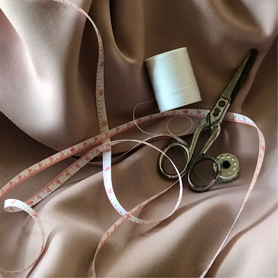 A pair of scissors and a roll of string laid out on a soft light brown fabric overlayed by measuring tape.