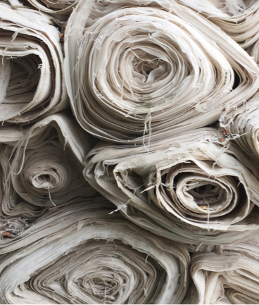 Stacks of uncoloured rolls of fabric.